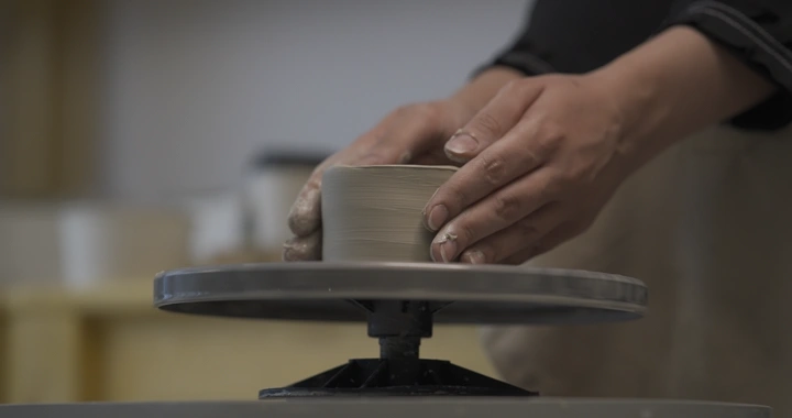 يد تصنع الفخار على عجلة دوارة في ورشة عمل، لقطة مقربة.