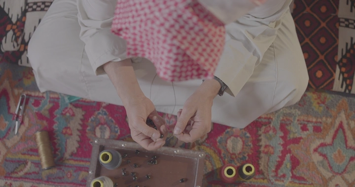 شخص يصنع سبحة يدوية على سجادة مزخرفة، لقطة علوية.