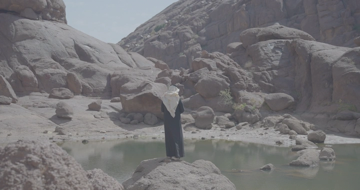 شخص يقف أمام بركة ماء صغيرة في جبال الكشرية بحائل، لقطة نهارية.