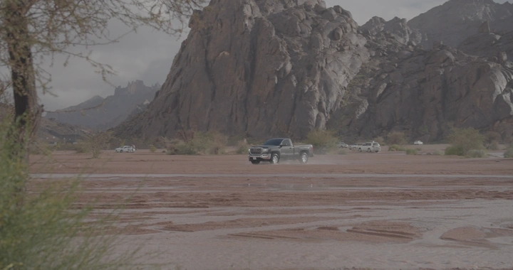 سيارة تسير على أرض موحلة أمام جبل في حائل، لقطة طبيعية.