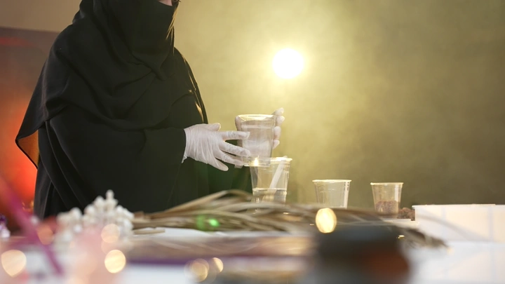 امرأة ترتدي عباءة تعمل على صنع تحف من الريزن، إضاءة خلفية.