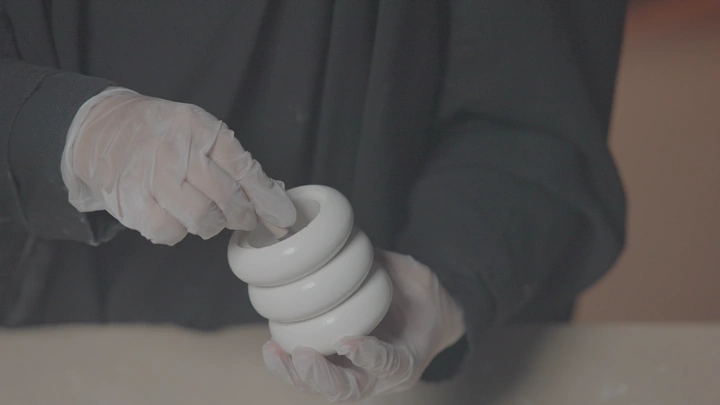 يد ترتدي قفازات تعمل على تشكيل الجبس في ورشة، لقطة مقربة.