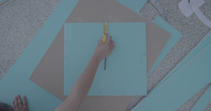 يد تقيس لوح خشب أزرق على الأرض، لقطة علوية.