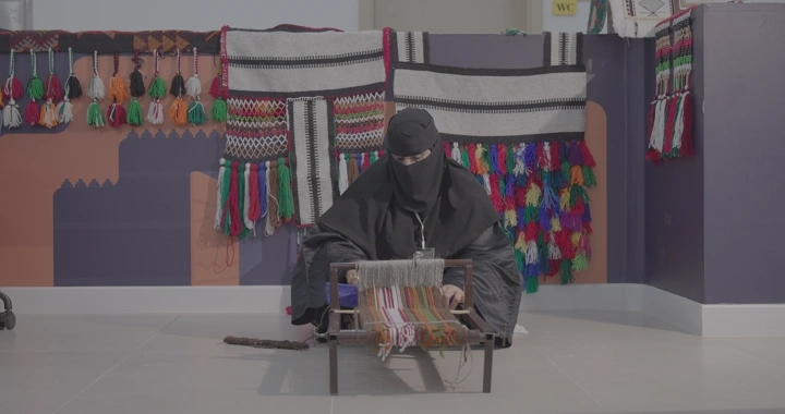 امرأة تعمل على نول السدو التقليدي في غرفة مزينة بالسدو، لقطة أمامية.