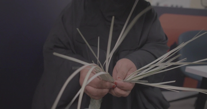 امرأة تنسج الخوص يدويًا في الداخل، لقطة مقربة.