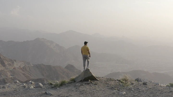 شخص يقف على صخرة في جبال الطائف، لقطة من الخلف.
