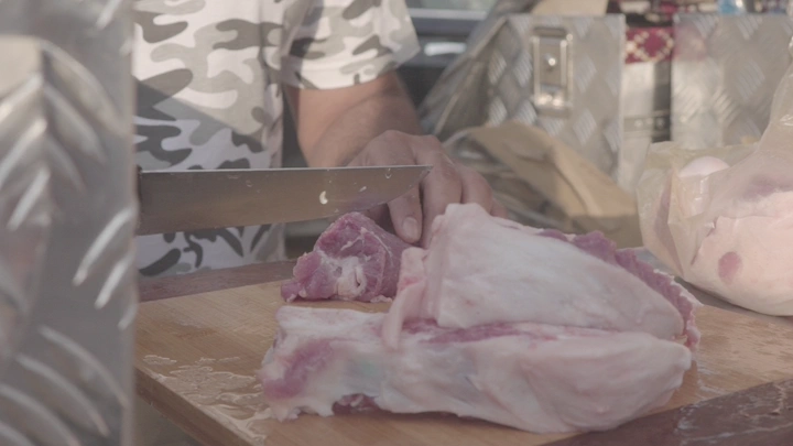 شخص يقطع اللحم على لوح خشبي في الهواء الطلق، لقطة مقربة.