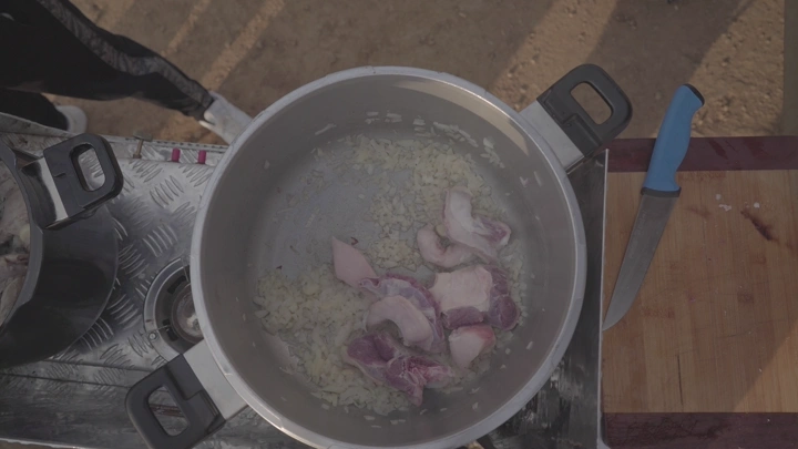 طبخ لحم وبصل في قدر على موقد خارجي، لقطة علوية.