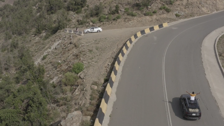 طريق عقبة حزنه في الباحة مع سيارة وشخص يرفع يديه، لقطة جوية.