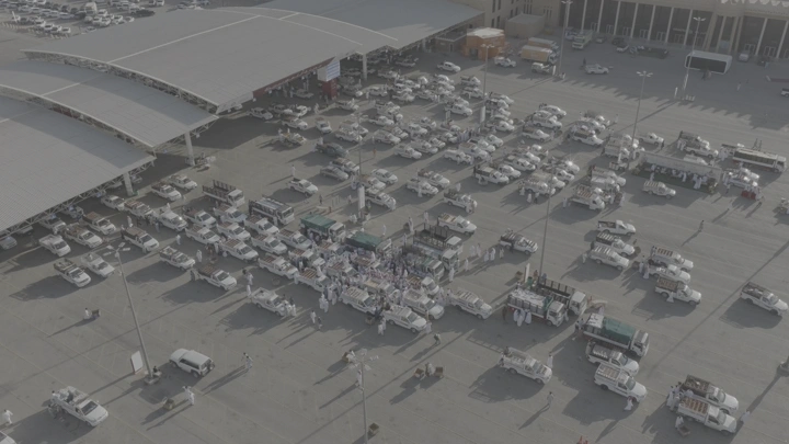 سوق التمر في القصيم، مشهد جوي نهاري يعرض السيارات والمظلات.