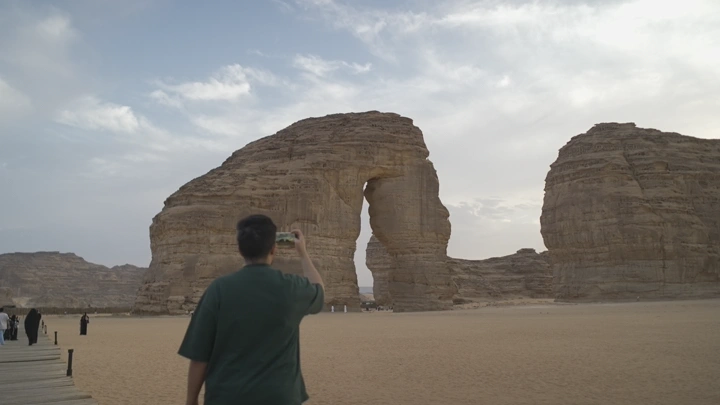 جبل الفيل في العلا خلال النهار، لقطة من الخلف لشخص يصور.