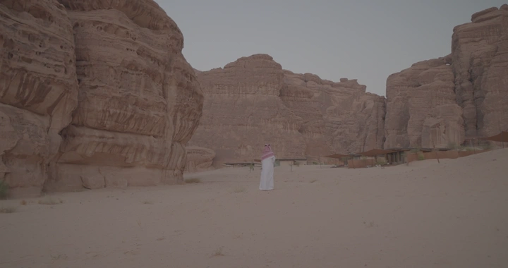 رجل في منتجع صحراوي محاط بتكوينات صخرية في العلا، لقطة بعيدة.