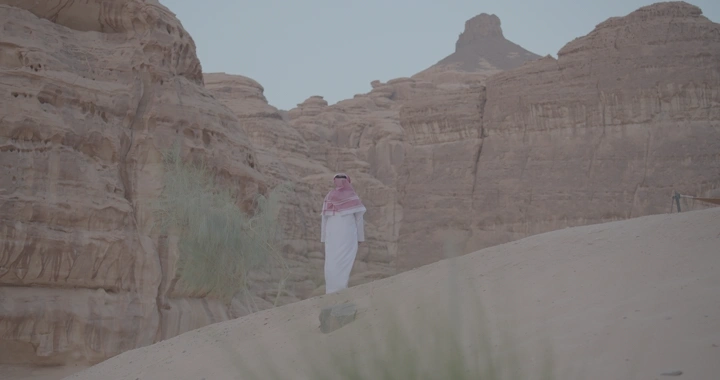 رجل يرتدي الزي السعودي يقف أمام جبال العلا، لقطة واسعة.