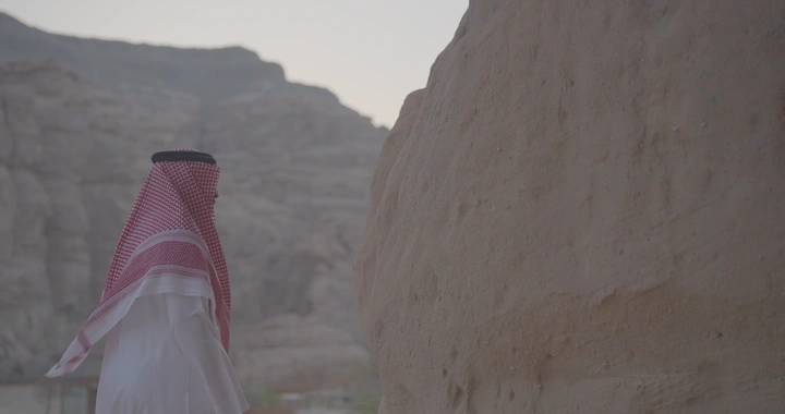 رجل بزي سعودي يقف أمام جبال العلا، لقطة جانبية.