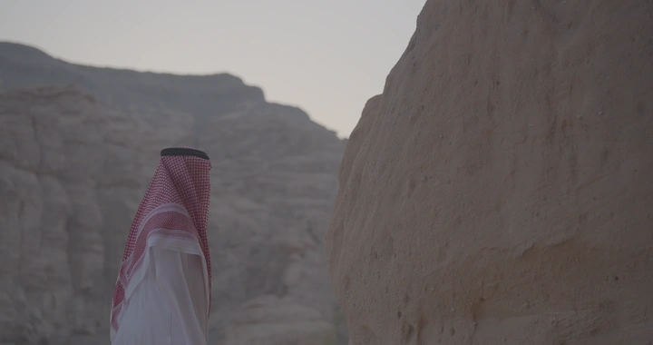 شخص يرتدي الزي السعودي يلمس صخرة في جبال العلا، لقطة جانبية.