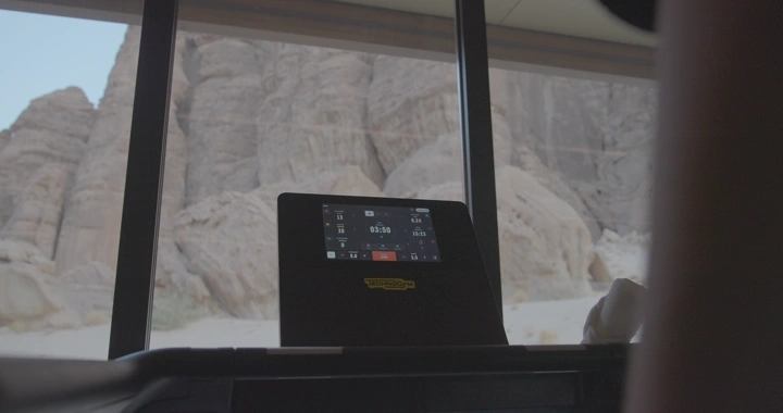 جهاز سير رياضي أمام نافذة تطل على جبال صخرية، لقطة داخلية.