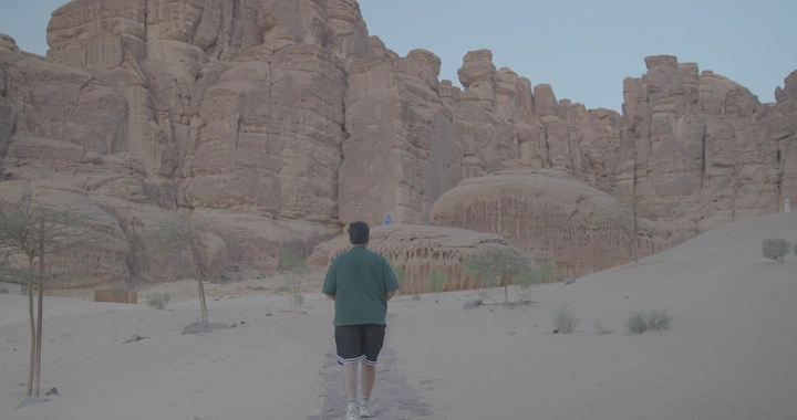 شخص يمشي نحو جبال العلا في الصحراء، لقطة من الخلف.