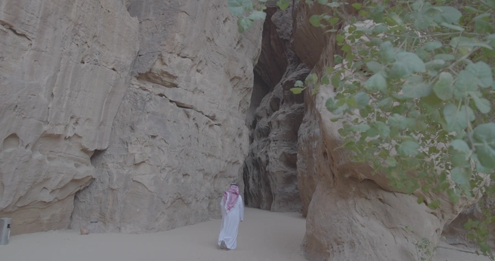 شخص يرتدي الزي السعودي يمشي في وادي جبلي بالعلا، لقطة طبيعية.