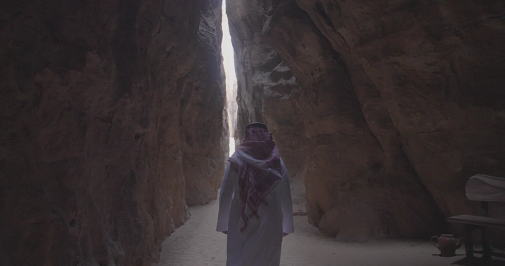 شخص يسير في ممر جبلي ضيق في العلا، لقطة من الخلف.