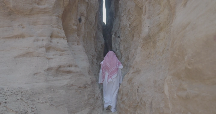 شخص يرتدي الثوب السعودي يسير بين جبال العلا، لقطة من الخلف.