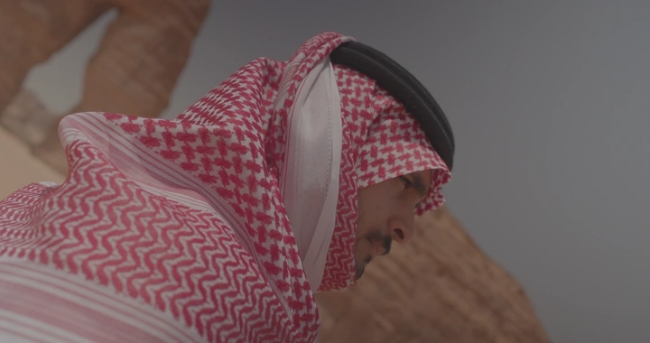 رجل يرتدي شماغًا أمام جبل الفيل في العلا، لقطة جانبية.