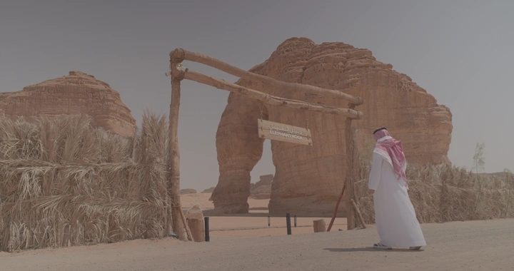 رجل يرتدي ثوبًا سعوديًا أمام جبل الفيل في العلا، لقطة نهارية.