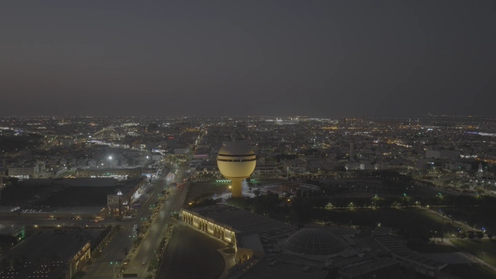 برج مياه بريدة مضاء ليلاً في القصيم، لقطة جوية.