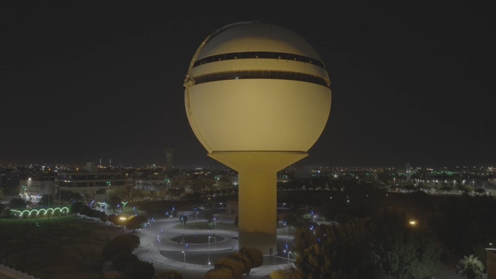 برج مياه بريدة مضاء ليلاً في القصيم، لقطة جوية.