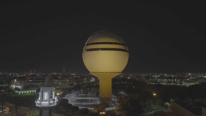 برج مياه بريدة مضاء ليلاً في القصيم، لقطة جوية.