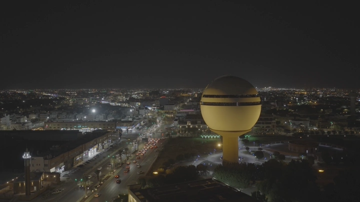 برج مياه بريدة مضاء ليلاً في القصيم، لقطة جوية.