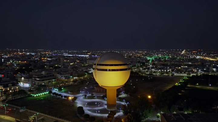 برج مياه بريدة مضاء ليلاً في القصيم، لقطة جوية.