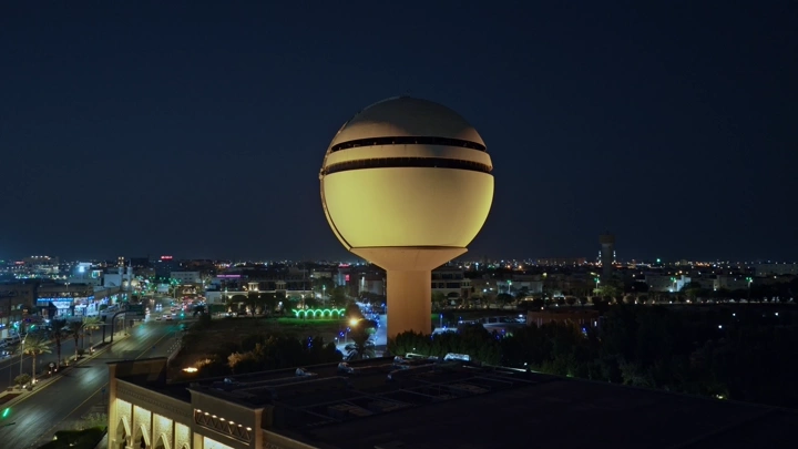 برج مياه بريدة مضاء ليلاً في القصيم، لقطة جوية.