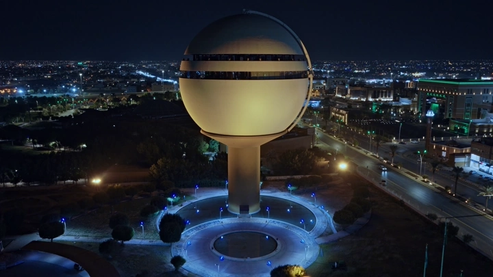 برج مياه بريدة مضاء ليلاً في القصيم، لقطة جوية.