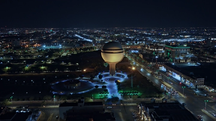 برج مياه بريدة مضاء ليلاً في القصيم، لقطة جوية.