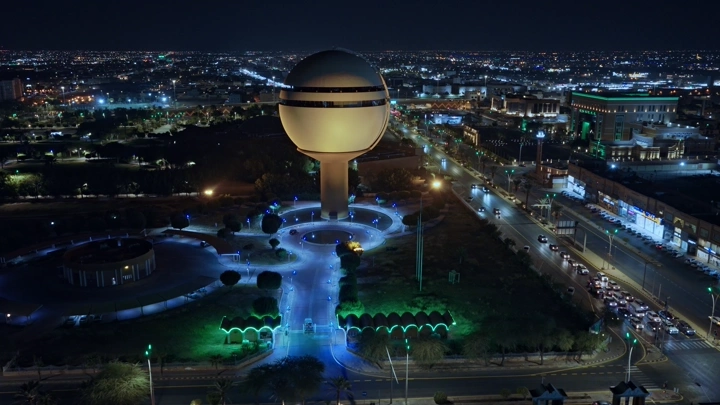 برج مياه بريدة مضاء ليلاً في القصيم، لقطة جوية.