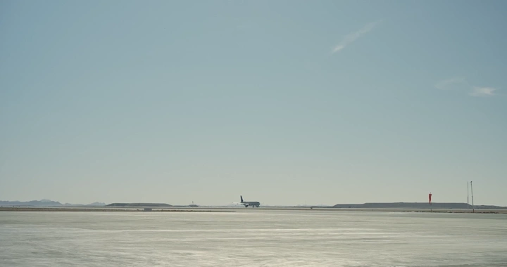 طائرة تقلع من مدرج مطار في يوم مشمس، لقطة بعيدة.