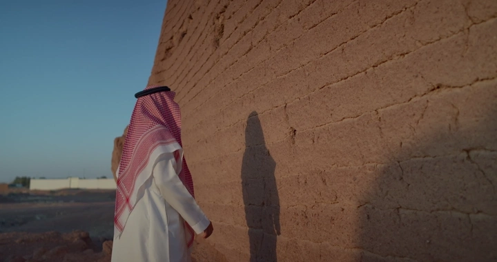 رجل سعودي يقف ويلمس جدار طيني في النهار، لقطة جانبية.