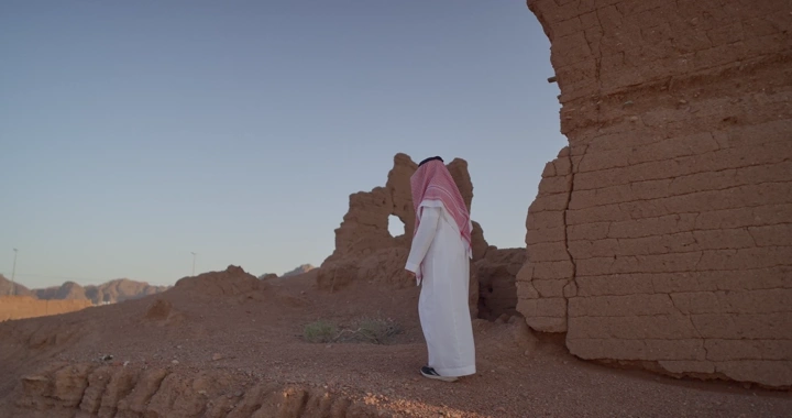 رجل سعودي يقف بجانب بيت طين في الصحراء، لقطة جانبية.