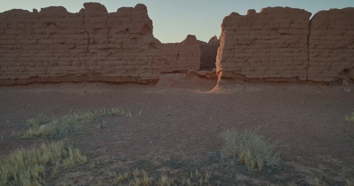 رجل يمشي عند جدار طيني قديم في الصحراء عند الغروب، لقطة أرضية.
