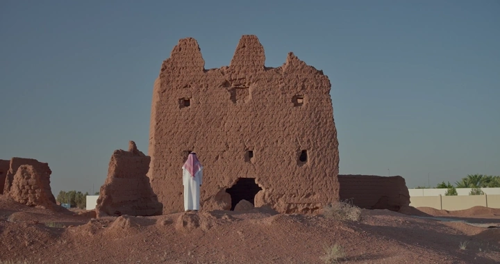 رجل يقف أمام بيت طيني قديم في الصحراء، لقطة نهارية.