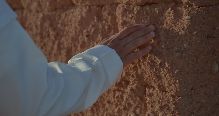 يد تلمس جدار طيني في ضوء النهار، لقطة مقربة.