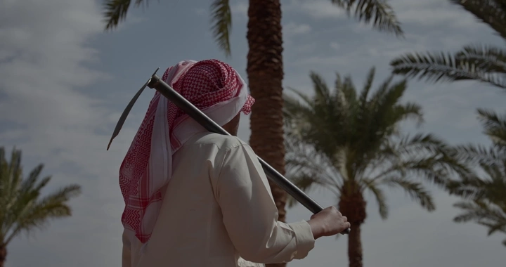 مزارع يحمل مجرفه في بستان نخيل، لقطة من الخلف.