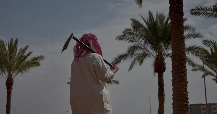 مزارع يحمل مجرفه بين أشجار النخيل، لقطة من الخلف.