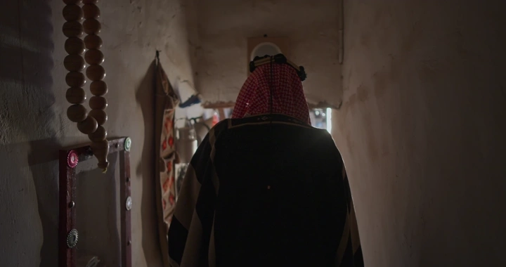 رجل يرتدي بشت سعودي في متحف تقليدي، لقطة من الخلف.