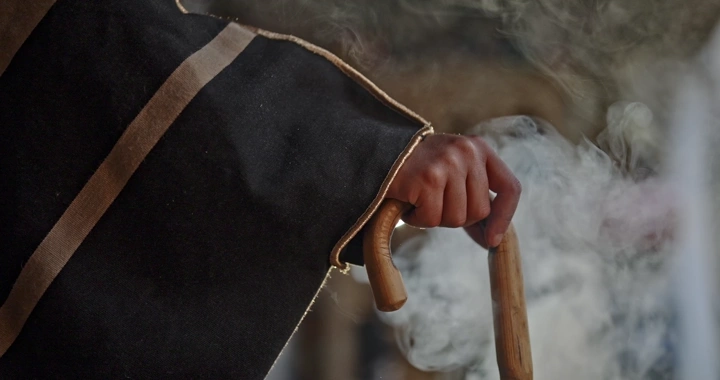 يد رجل تحمل عصا مع بشت ودخان النار، لقطة قريبة.