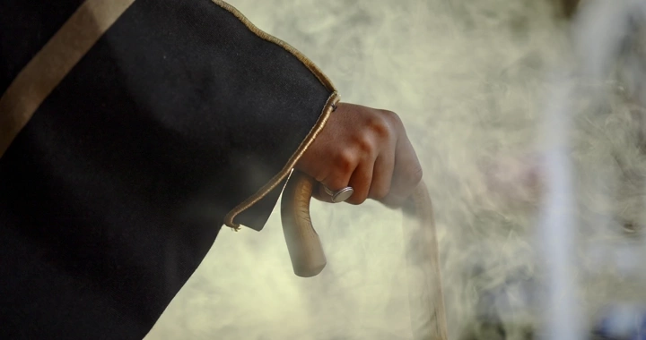 يد رجل يمسك عصا ويرتدي بشت، لقطة مقربة.