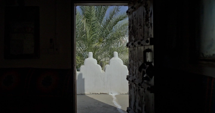 منظر من داخل بيت طين يظهر نخلة في الخارج، لقطة من الباب.