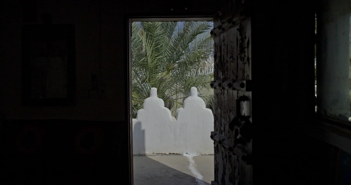 باب مفتوح يطل على نخيل في بيت طيني، لقطة داخلية.