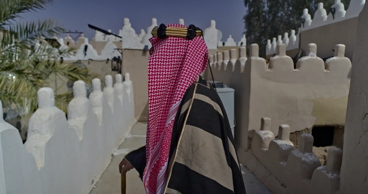 رجل يرتدي بشت سعودي في بيت طيني، لقطة جانبية.