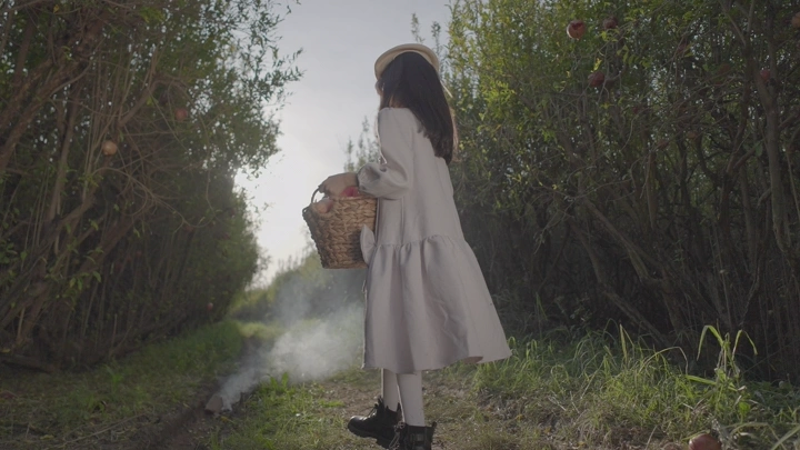 طفلة تحمل سلة في مزرعة رمان، لقطة من الخلف.